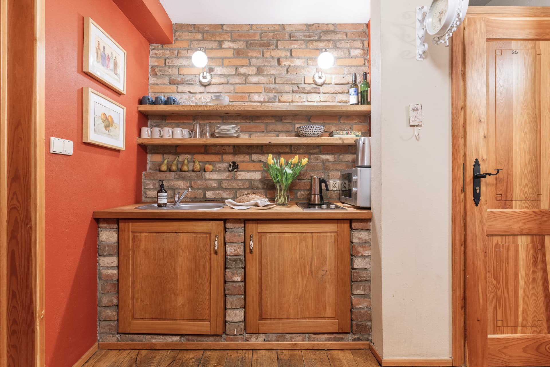 Compact kitchenette alcove with open timber shelves, a sink and a two-burner hob