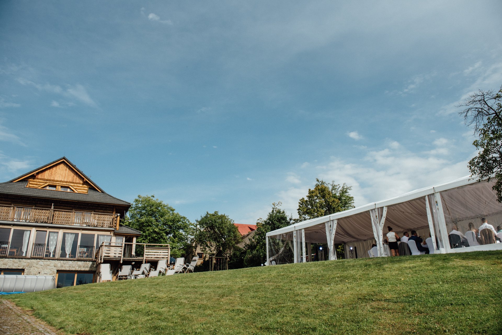 The timber lodge with a white wedding marquee set up on the grassy slope