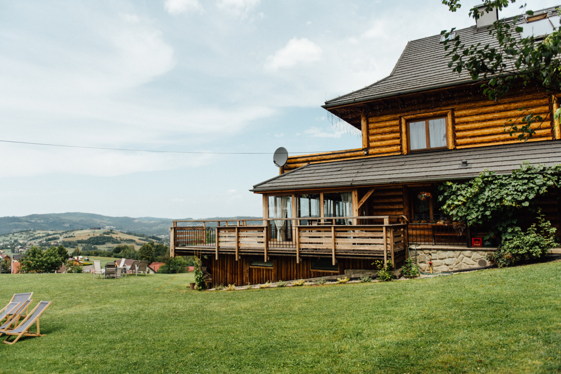 The lodge in summer, with the balcony, glazed veranda and deck chairs on the lawn