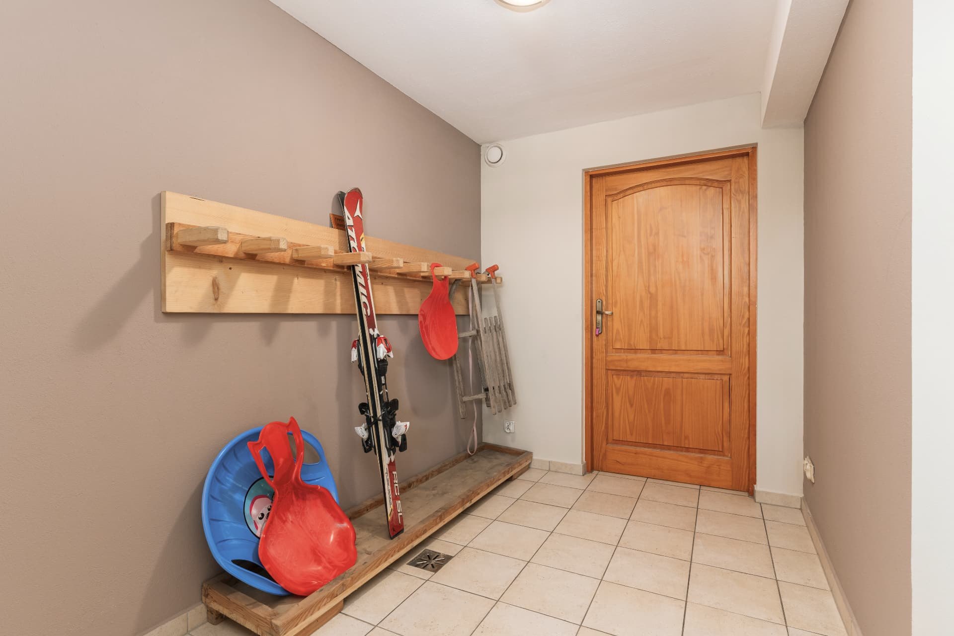 Ski storage with skis, plastic sledges and a wooden sled on a wall rack