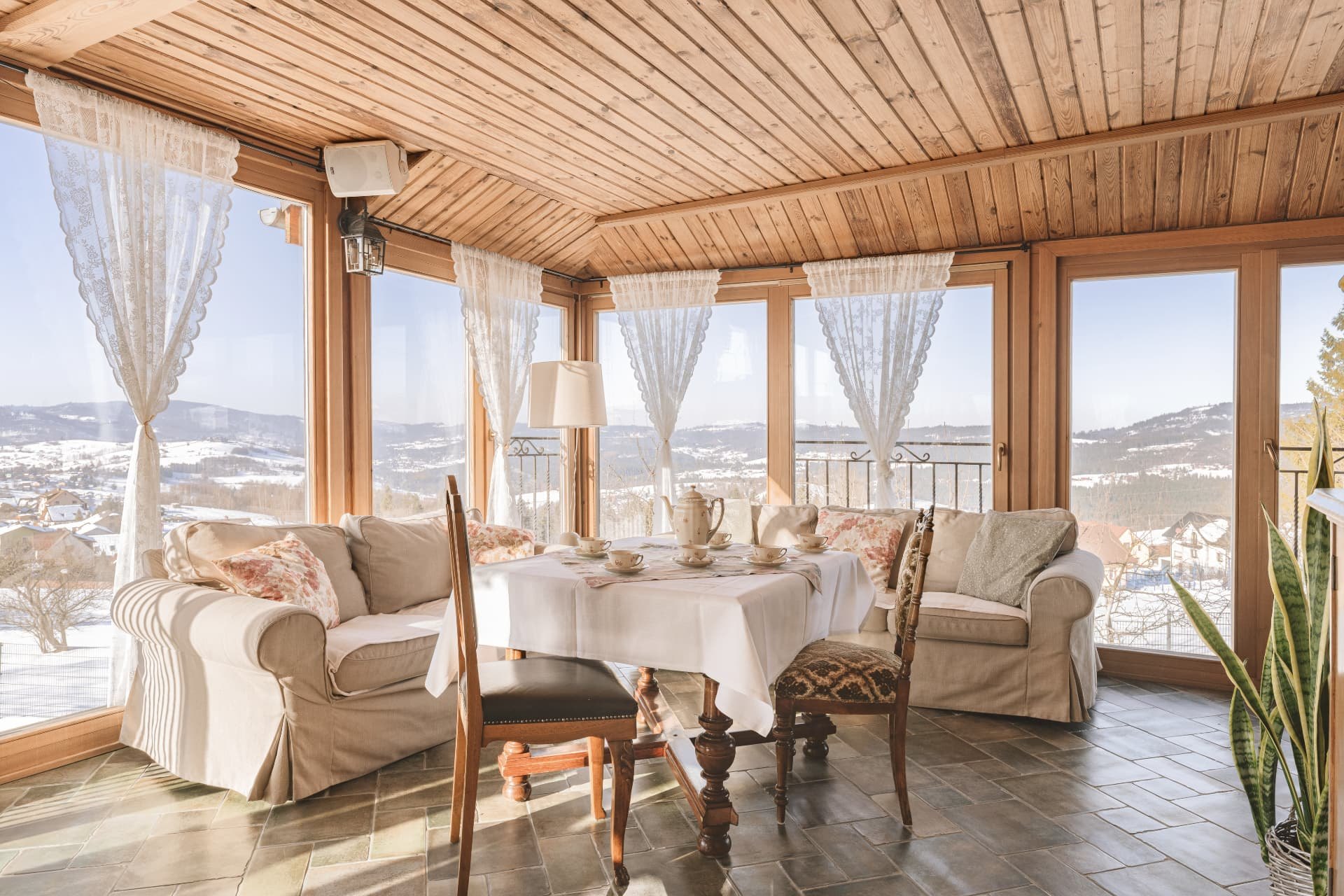 Sunroom with cream sofas and a tea table set before windows onto the snowy valley