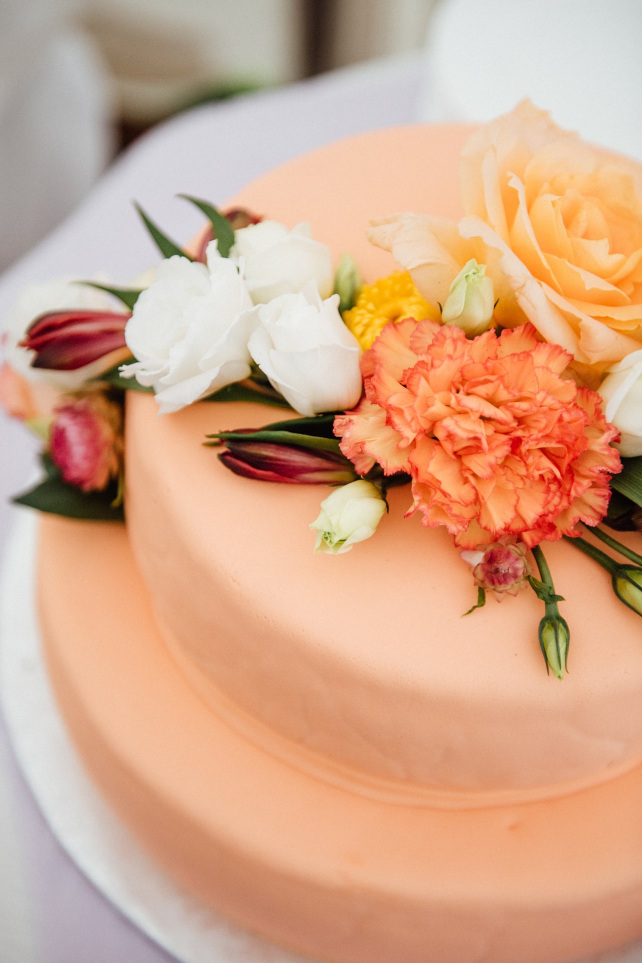 Tiered peach wedding cake decorated with fresh roses and carnations