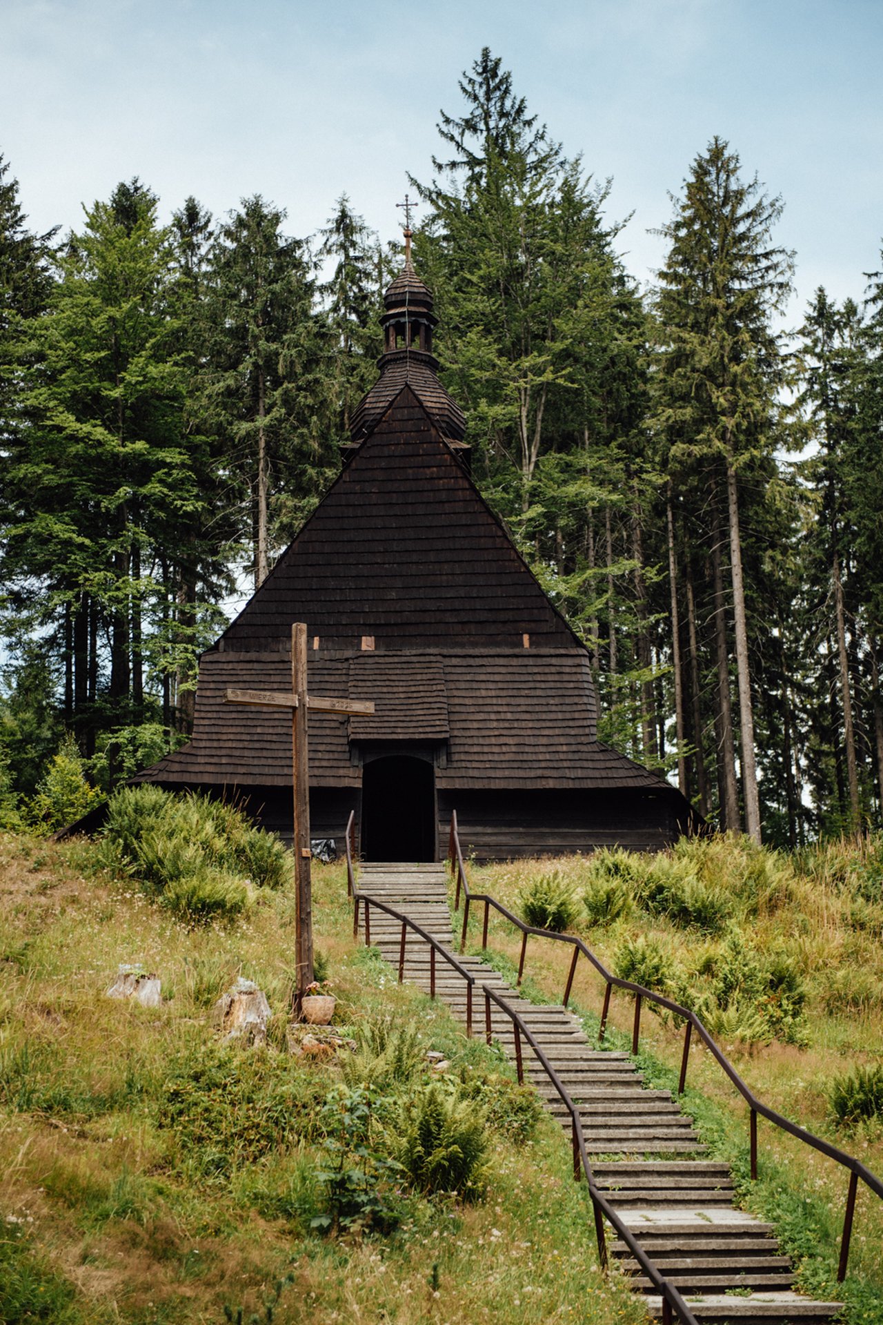 Historic wooden chapel in the pine forest with stone steps and a wooden cross