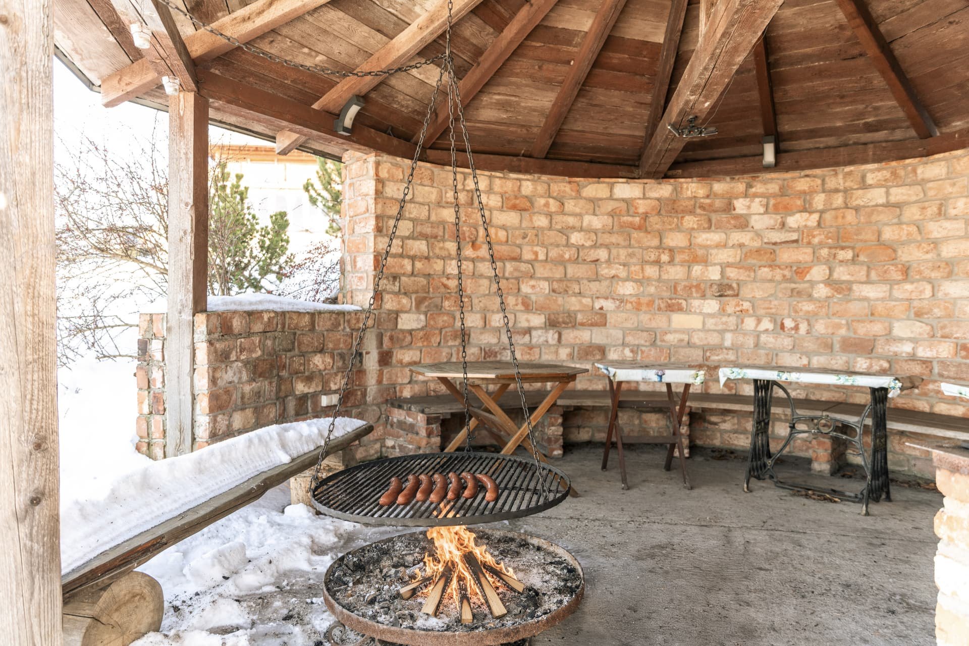Sausages grilling over an open fire in the covered wooden gazebo