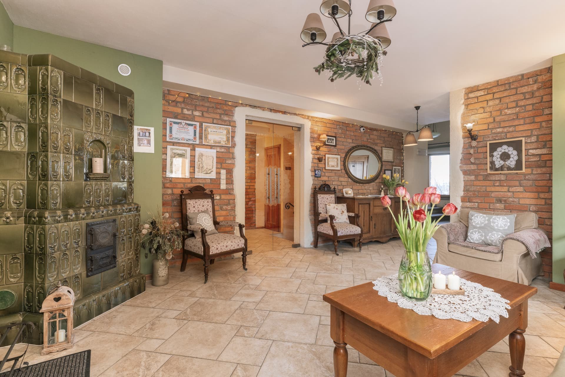 Lounge with a traditional green tile stove, brick walls and tulips on the table