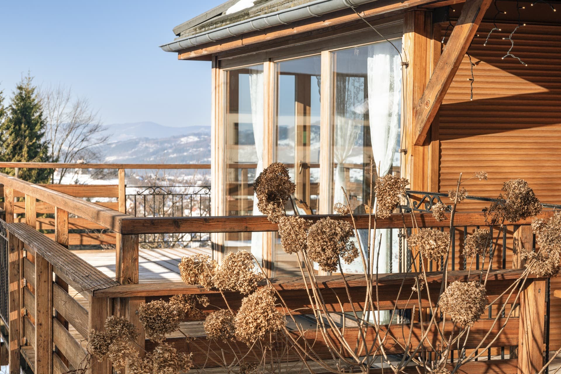Wooden balcony deck toward the glazed sunroom, with snow-covered hills beyond the railing