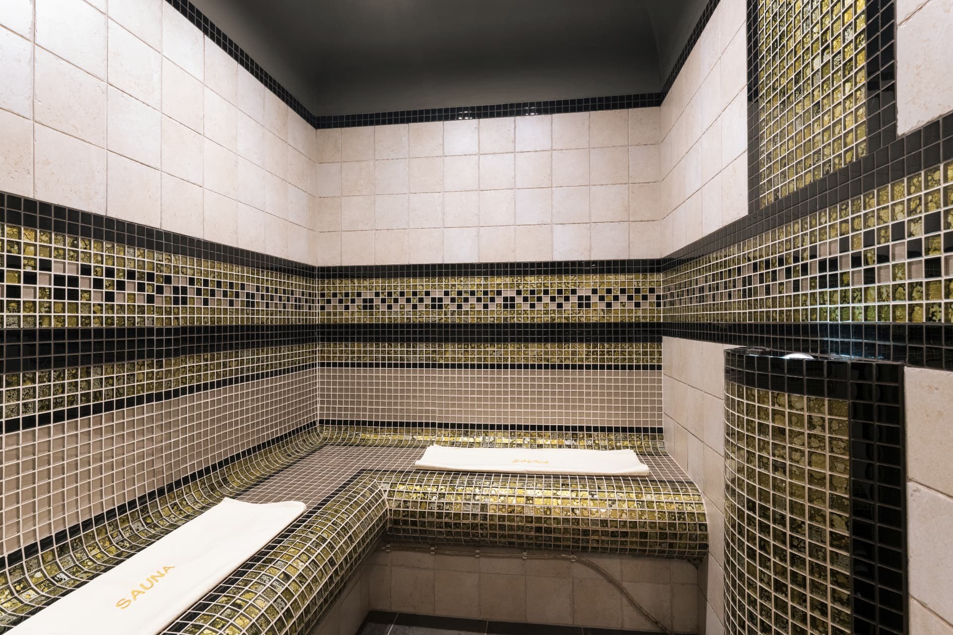 Mosaic steam bath with curved tiled benches and folded towels