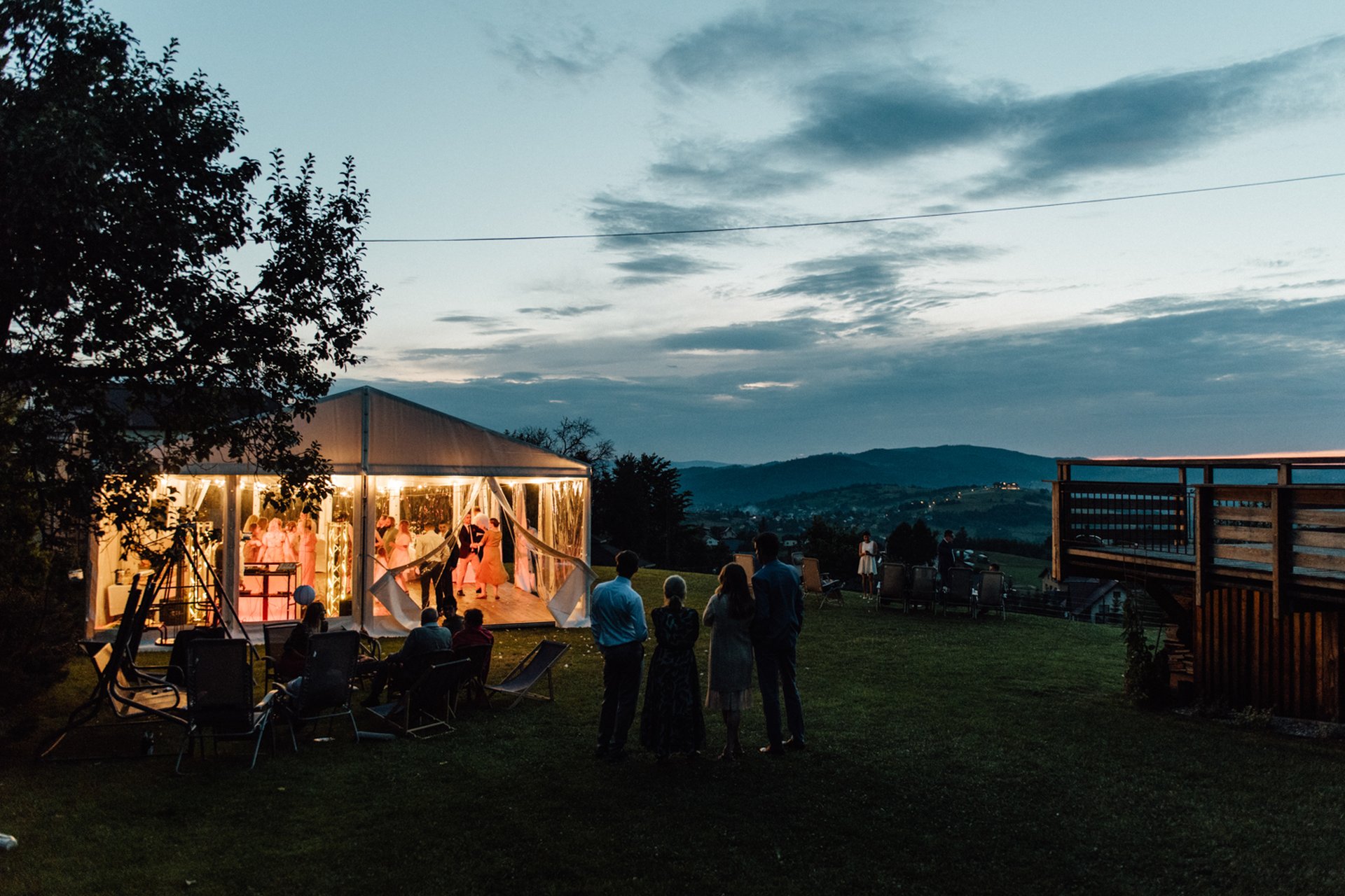 Wedding reception tent lit at twilight on the lawn with mountain views beyond