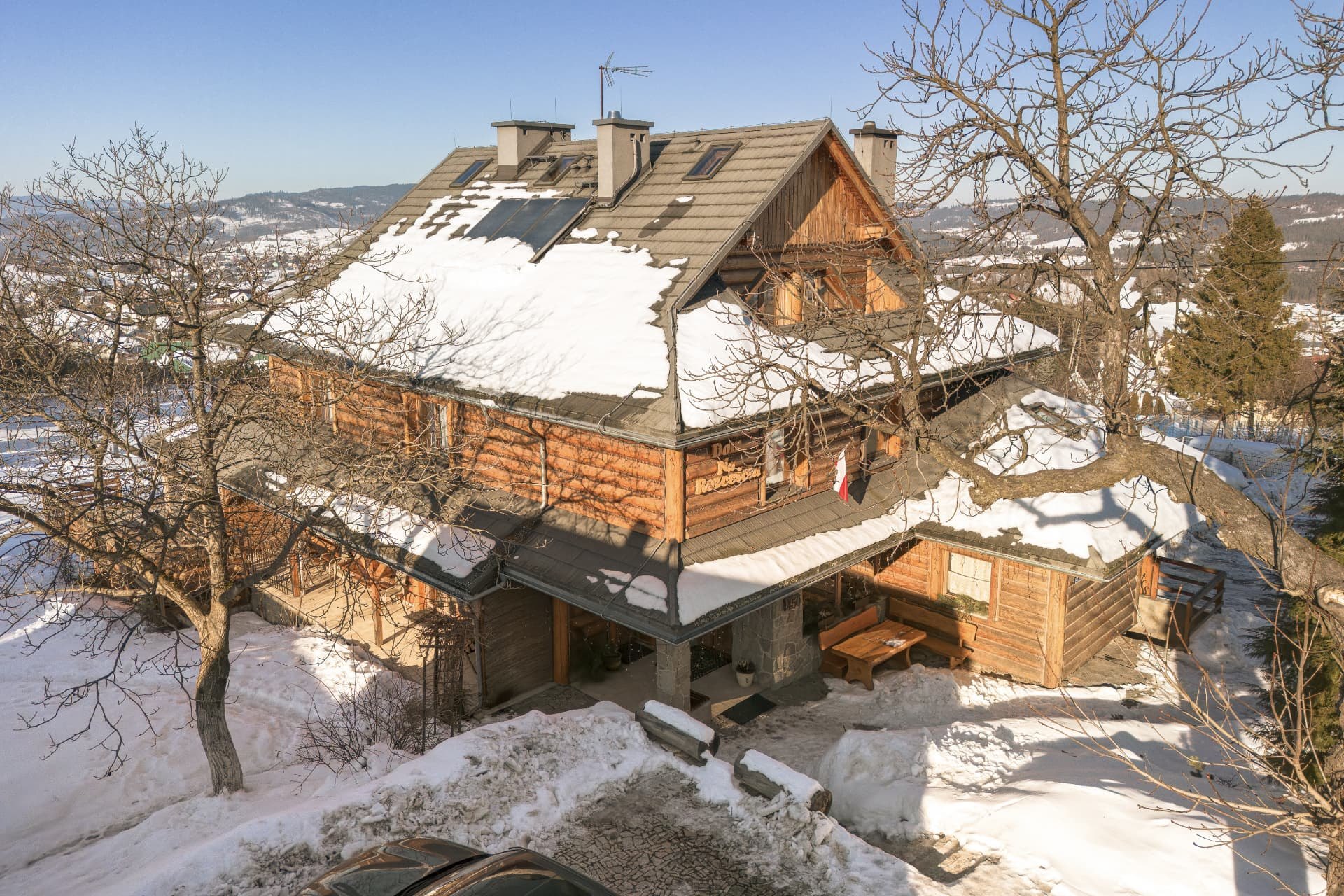 The lodge from the drive in winter, with snow on the roof and a covered terrace with benches